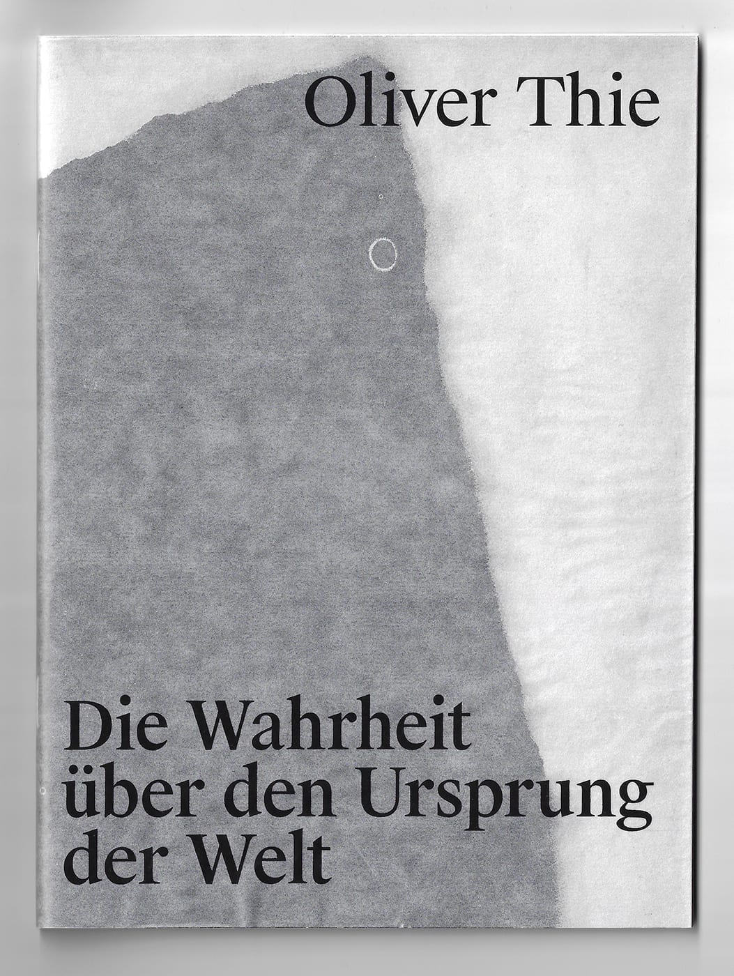 Titelseite eines Buches von Oliver Thie. Vor einem weißen Hintergrund zieht sich eine große, unregelmäßige graue Fläche vertikal über die linke Bildhälfte. Ihre weichen, ausgefransten Ränder erinnern an einen Abdruck, eine Spur oder eine fragmentarische Materialoberfläche. Im oberen Bereich steht der Name „Oliver Thie“ in großer schwarzer Schrift. Im unteren linken Bereich ist der Titel Die Wahrheit über den Ursprung der Welt in großer schwarzer Schrift angeordnet. Die reduzierte Gestaltung aus Weiß, Grau und Schwarz wirkt ruhig, offen und leicht rätselhaft.