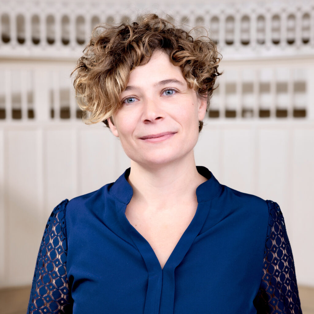 Bust Portrait of Paz Ponce, Curator Outreach and Public Programmes. She is wearing a blue shirt and is standing in the auditorium of Tieranatomisches Theater. 